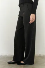 Pantalón negro de corte amplio con cintura alta, cierre de cremallera y botón. Cuenta con bolsillos laterales y tela bordada.
