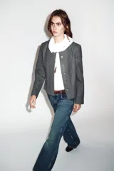 Blazer de corte entallado con cuello redondo, manga larga y hombreras. Presenta cierre frontal con botones dorados y una textura sutil en la tela.