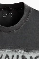 Remera deportiva de corte boxy y holgado con tecnología DryMove, en color gris oscuro con efecto gastado. Presenta hombros caídos, cuello redondo ribeteado y un gran estampado frontal en tonos claros con la palabra 'RUNNING' y siluetas de personas corriendo.
