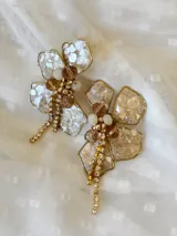 Aros colgantes con forma de flor, pétalos de resina color champagne con borde dorado, centro con cuentas de cristal color ámbar y blanco, y flecos de strass dorados.