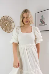 Vestido corto blanco de tela arrugada, con escote cuadrado, mangas abullonadas con volados y falda escalonada con volados.