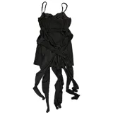 Vestido corto negro de corte asimétrico con escote en V y tirantes finos. Presenta un diseño con efecto desgastado y una sobrefalda con lazo frontal que aporta volumen y movimiento.