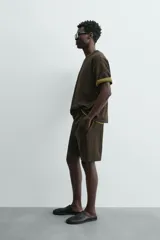 Sudadera de manga corta con cuello redondo, confeccionada en tejido texturizado de color verde oscuro/marrón. Presenta un corte relajado (relaxed fit).