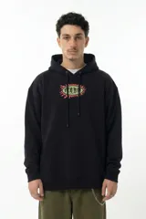 Hoodie negro de corte relajado con capucha y cordones ajustables. Presenta un estampado gráfico central en el pecho con forma ovalada y bordes irregulares en tonos verde y rojo.