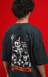 Remera de algodón premium color carbón, corte oversize, con cuello redondo y manga corta. Presenta un estampado frontal con calaveras en estilo caricaturesco, una de ellas con sombrero de copa, rodeadas de humo o nubes, y el texto "CHILLED THE BONE".