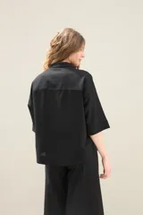 Camisa de lino de calce relajado, color negro, con cuello mao, mangas cortas y bajo redondeado con aberturas laterales.