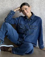 Sobrecamisa de denim azul con cuello camisero, cierre frontal con botones, mangas largas con puños abotonados y dos bolsillos con solapa en el pecho.