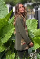 Saco de lana color verde militar con estampado abstracto en tonos verde oliva y detalles bordados en rojo. Tiene cuello solapa, cierre frontal con botones de madera y puños acanalados.