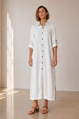 Vestido largo tipo chemise color blanco, con cuello camisero, cierre frontal de botones, bolsillos laterales y mangas tres cuartos con vuelta.