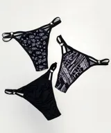 Pack de tres bombachas colaless con tiras finas y argollas metálicas. Incluye una bombacha negra lisa, una con estampado de flores blancas y otra con estampado abstracto en blanco y negro.