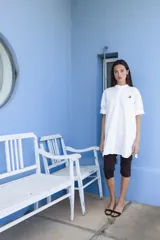 Camisa blanca de corte oversize y largo midi, confeccionada en algodón. Presenta cuello mao, cierre frontal oculto por tapeta y mangas cortas con dobladillo. Incluye un pequeño bordado de una flor en el pecho.