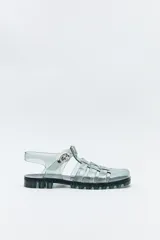 Sandalias jelly color gris translúcido, con diseño entrecruzado y hebilla lateral ajustable.