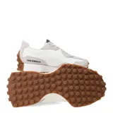 Championes urbanos New Balance modelo 327, con diseño retro inspirado en los años 70. Presentan una combinación de paneles de gamuza gris claro y base de nylon blanco, con el logo 'N' sobredimensionado en cuero sintético negro en el lateral. Incluyen una entresuela de espuma blanca y una suela de goma dentada que se extiende hacia el talón.