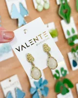 Aros colgantes dorados con pieza superior texturizada y dije inferior en forma de lágrima con piedra blanca.