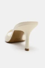 Sandalia de tacón tipo mule color beige, con tira ancha delantera, tacón fino alto y punta redondeada.
