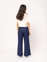 Pantalón de lino color beige, de tiro alto, pierna ancha y levemente acampanada. Tiene pinzas delanteras, elástico en la pretina trasera, cierre delantero y broche interno, bolsillos laterales y dobladillo invisible.