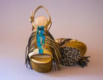 Sandalias de cuero dorado con plataforma de madera, taco alto, flecos prominentes y detalle frontal de cuero pintado a mano en tonos turquesa y cobre.
