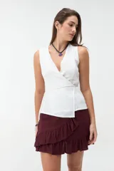 Chaleco blanco cruzado sin mangas, con escote en V y lazo ajustable en la cintura.