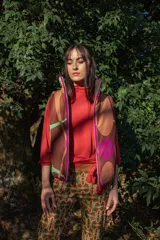 Chaleco puffer con estampado abstracto en tonos marrones, verdes y fucsia. Tiene cuello alto, cierre frontal con cremallera y ribete fucsia.