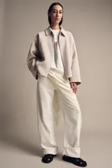 Chaqueta de lana en color beige, con cuello solapa, cierre frontal con cremallera metálica, mangas largas con corte evasé y bajo asimétrico.