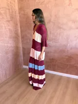 Vestido largo de tejido de punto con diseño a rayas horizontales en tonos bordó, crema, rosa y celeste. Presenta cuello polo con escote en V y mangas cortas con textura acanalada.