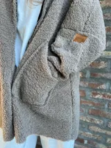 Campera de corderito color verde oscuro, con diseño holgado, cuello alto y manga larga. Presenta una etiqueta de cuero sintético en la manga.