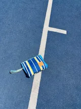 Sobre de mano azul con rayas verticales blancas y amarillas, con parche de cuero sintético marrón.