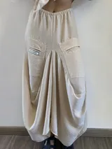 Pollera midi de corte asimétrico y holgado, inspirada en la forma de pantalón babucha. Confeccionada en tela crepé color beige, presenta cintura elástica, bolsillos laterales amplios y un detalle de etiqueta con texto en el bolsillo derecho.