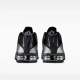 Championes Nike modelo Shox R4, con diseño futurista que combina paneles de cuero sintético negro y plateado metálico. Presenta la icónica tecnología de amortiguación Shox en el talón con columnas plateadas y el logo de Nike en el lateral.