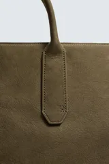 Bolso tipo bandolera de piel con acabado abatanado, diseño rectangular con doble asa de mano y detalle de llavero colgante. Cuenta con compartimento principal con cierre de mosquetón y bolsillo interior con cremallera.