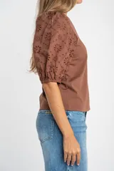 Remera de algodón color rosado con mangas cortas abullonadas de broderie con diseño floral calado. Presenta cuello redondo y costura vertical central en el frente.