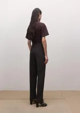Pantalón de sastre color marrón oscuro, de corte recto y tiro medio, con bolsillos laterales y raya central marcada.