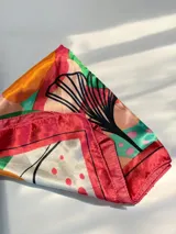 Pañuelo cuadrado de seda con estampado floral multicolor que combina tonos rojos, amarillos, azules y fucsias sobre fondo blanco, con borde rojo.