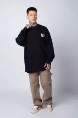 Buzo de tejido friza color crema, de corte oversize y cuello redondo. Presenta un pequeño bordado o parche en el pecho izquierdo con un diseño de cabeza de animal en tonos rojizos/terracota.