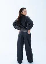 Campera rompeviento negra de estilo deportivo, con cierre frontal completo, cuello alto y detalles de líneas blancas en los hombros y mangas. Presenta puños y cintura elásticos en tono gris oscuro.
