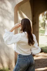 Blusa blanca de lino con mangas largas abullonadas, escote en V con lazo de ajuste frontal y detalles de puntilla en los bordes.