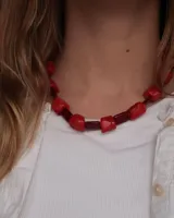 Collar corto de cuentas, alternando piezas grandes irregulares de color rojo vivo con cuentas cilíndricas más oscuras.
