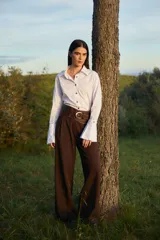 Camisa blanca de algodón con cuello clásico, cierre frontal de botones y puños anchos desmontables. Presenta un diseño con tablas decorativas y terminación redondeada en los laterales.