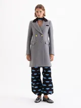 Tapado gris de paño con cuello de gamuza color chocolate. Diseño de doble botonadura con botones metálicos combinados, bolsillos con tapa en el delantero y solapa marcada. Largo hasta la rodilla, corte entallado y hombros levemente marcados.