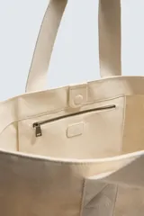 Bolso tipo shopper de tejido de algodón color beige claro, con dos asas de mano y cierre magnético en el compartimento principal. Incluye un bolsillo interior con cierre de cremallera.