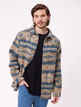 Camisa de manga larga con diseño de estampado étnico en tonos azules y beige. Presenta cuello clásico, cierre frontal con botones y bolsillos en el pecho.