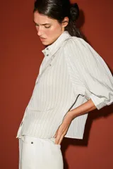 Camisa blanca a rayas sutiles, de cuello solapa y manga abullonada por debajo del codo. Presenta delicados bordados florales perforados en el frente y cierre frontal con botones.