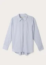 Camisa de manga larga en color celeste con estampado de rayas verticales finas. Presenta cuello clásico, cierre frontal con botones ocultos y puños con botones. El diseño tiene un corte recto con el ruedo trasero ligeramente más largo y redondeado.
