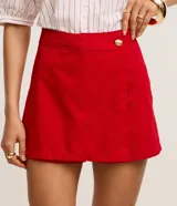 Short pollera de cintura alta confeccionado en sarga de algodón, con diseño de traspase tipo sobre y detalle de botón dorado en el frente.