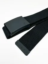 Cinturón de sarga marca Rusty, color negro, con hebilla metálica rectangular y puntera metálica grabada con el logo de la marca.