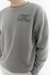 Buzo gris de algodón con corte oversize, cuello redondo y puños y cintura acanalados. Estampa frontal con texto "Manage Your Resistance" en letras de estilo graffiti.