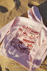 Hoodie rosa claro con estampado gráfico en la espalda en color rojo oscuro. El estampado incluye texto como "GLASSY WAVES SURF COMPANY", ilustraciones de bebidas, frutas, una tabla de surf y palmeras.