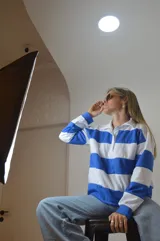 Sweater de punto a rayas horizontales azules y blancas, con cuello polo y cierre parcial con cremallera.