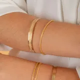 Esclava rígida de oro 18k con acabado satinado y diseño de cinta plana. Presenta una textura fina en su superficie y un diseño minimalista.