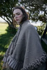 Ruana de tejido con textura en color bordó, con diseño amplio y fluido. Presenta detalles de volados aplicados en el cuello y ruedo, terminaciones con flecos y lazo frontal regulable.